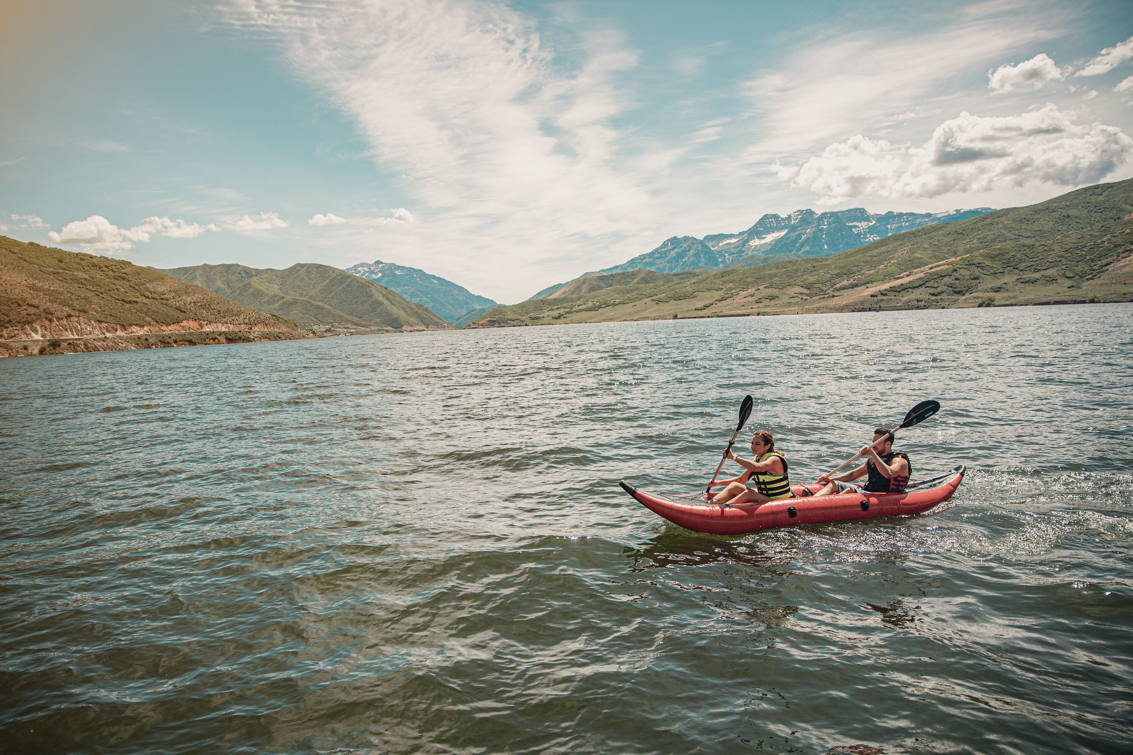 Un kayak con due persone che pagaiiano su un lago tranquillo, circondato dalle montagne.