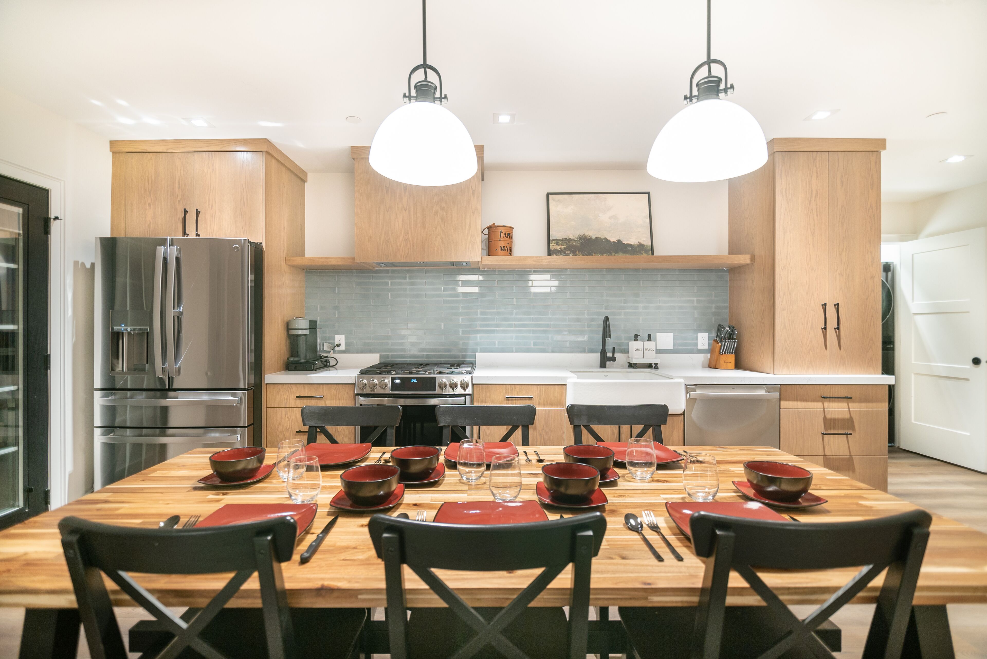 Una cocina moderna con armarios de madera, un refrigerador de acero inoxidable y una mesa de comedor para seis personas con individuales rojos y sillas negras.