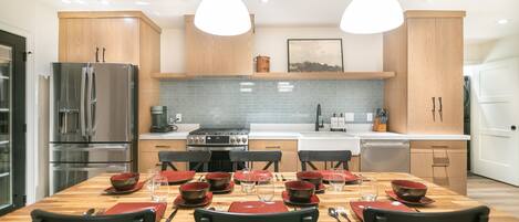 A modern kitchen with wooden cabinets, a stainless steel refrigerator, and a dining table set for six with red placemats and black chairs.
