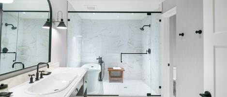 A modern bathroom with a large mirror, two sinks, a shower, and a small wooden stool.