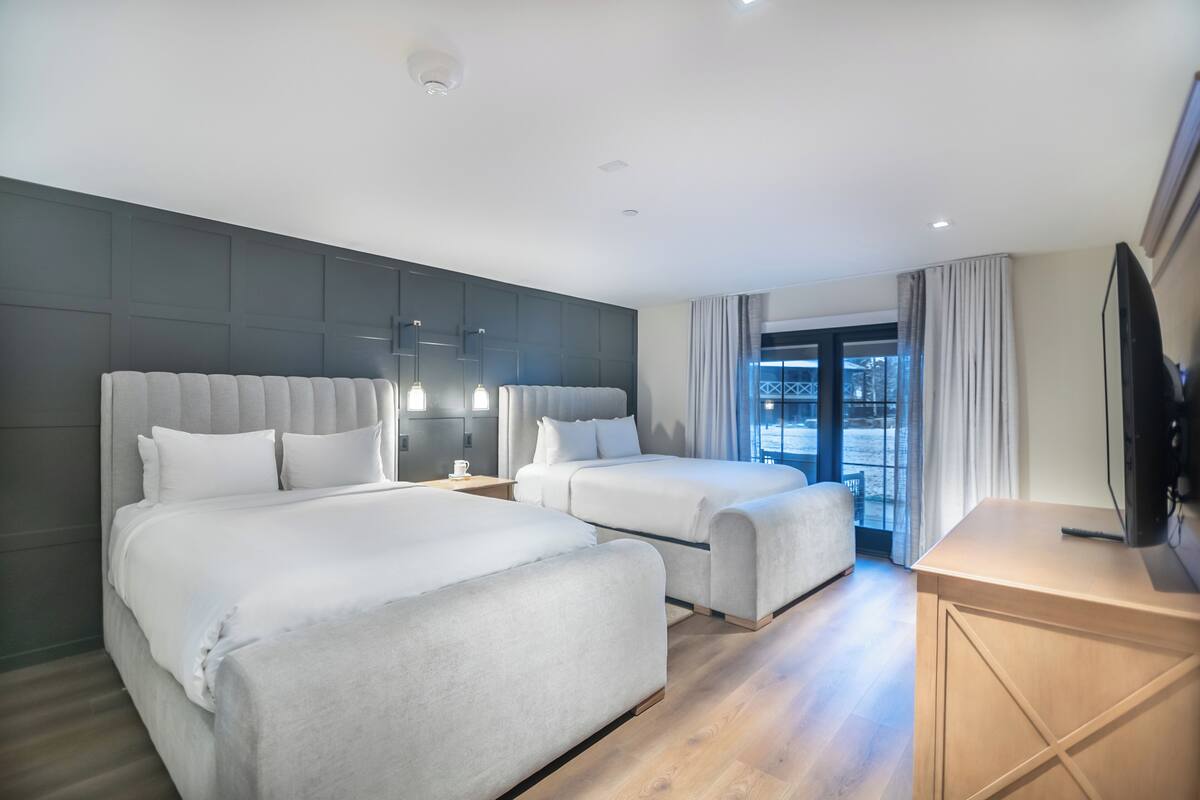 Ein modernes Hotelzimmer mit zwei Betten, einem Flachbildfernseher und einem großen Fenster mit Vorhängen.