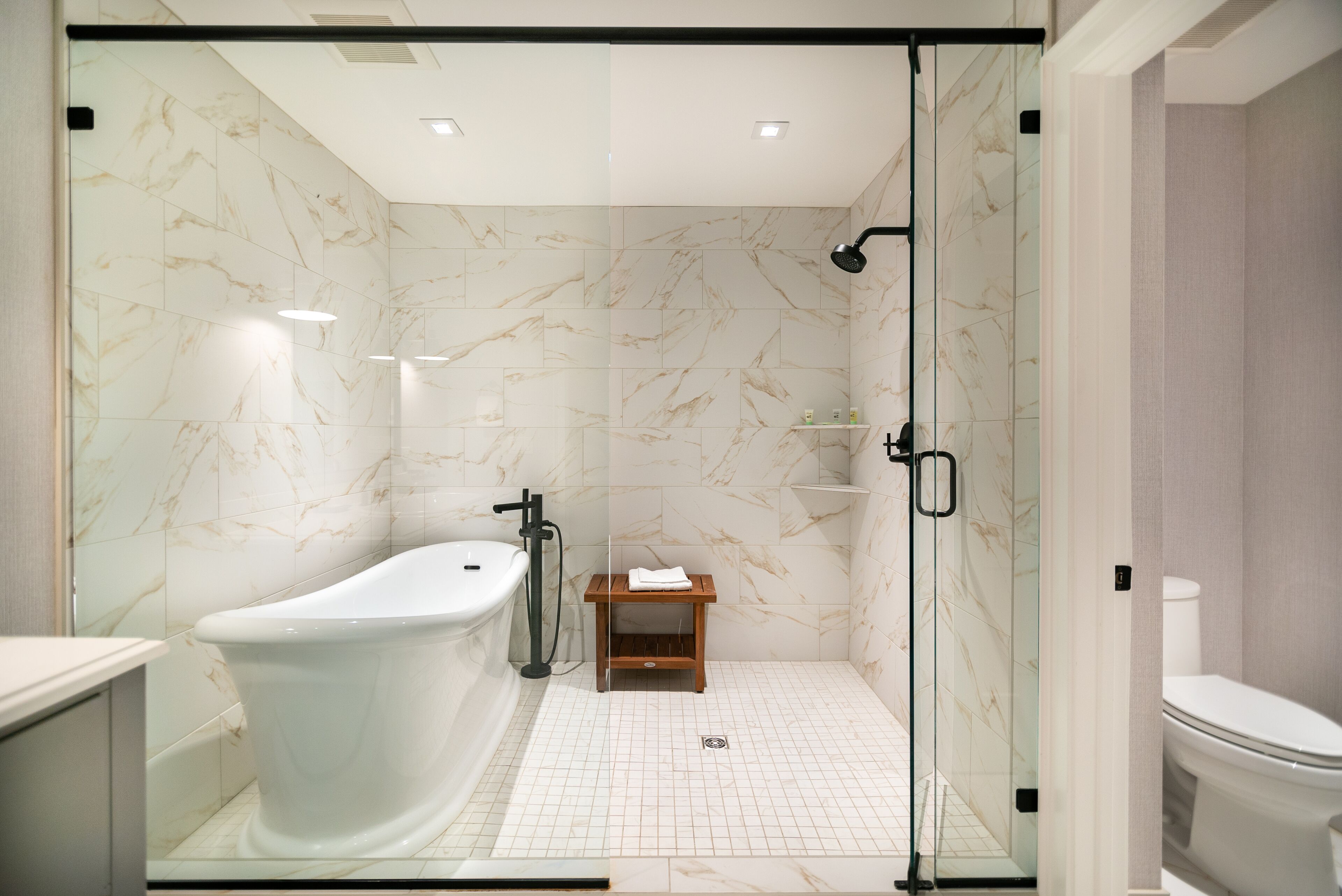 A modern bathroom with a freestanding bathtub, a glass-enclosed shower area, and a small wooden stool.