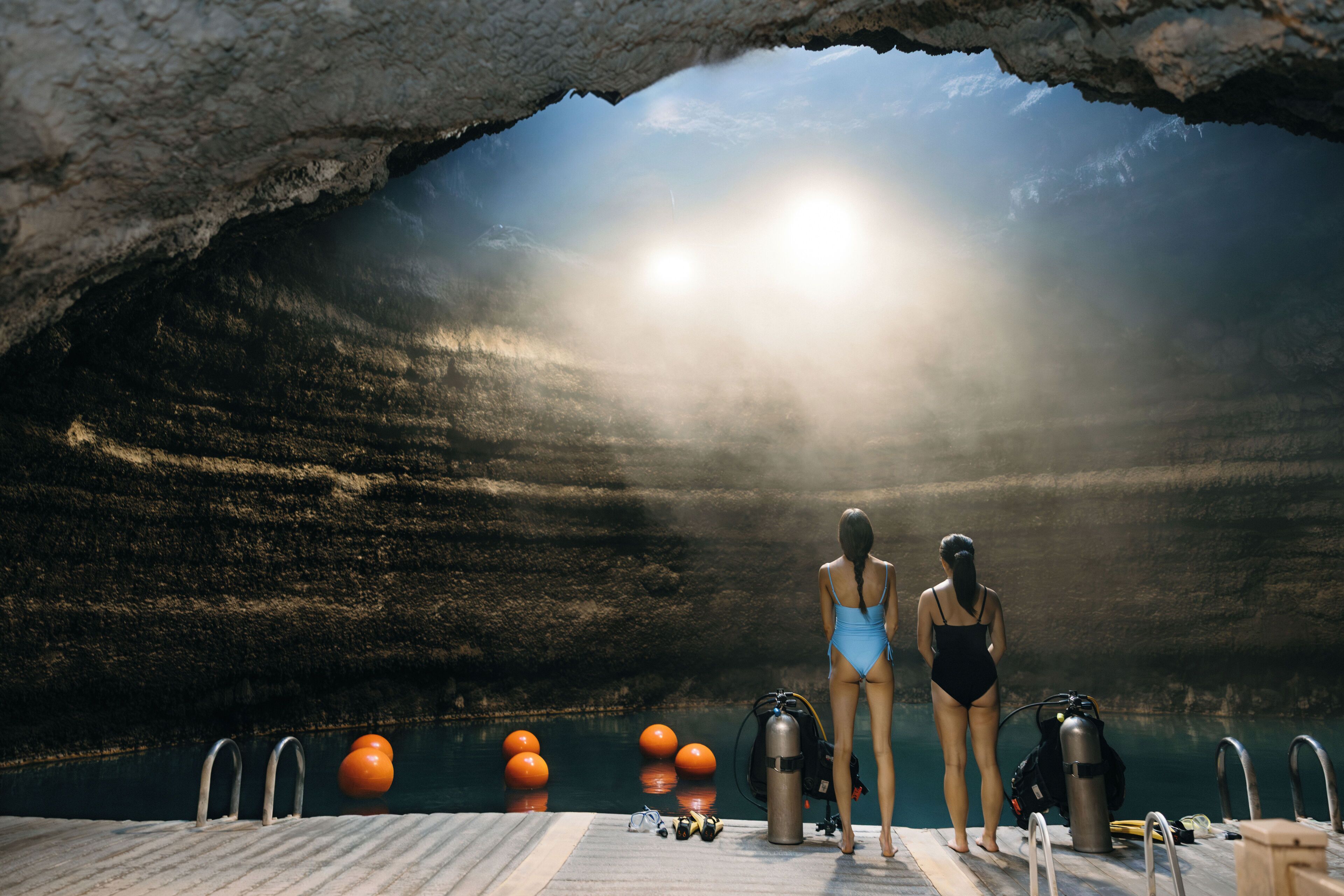 A diver standing at the edge of a pool with a rocky cave-like structure above.
