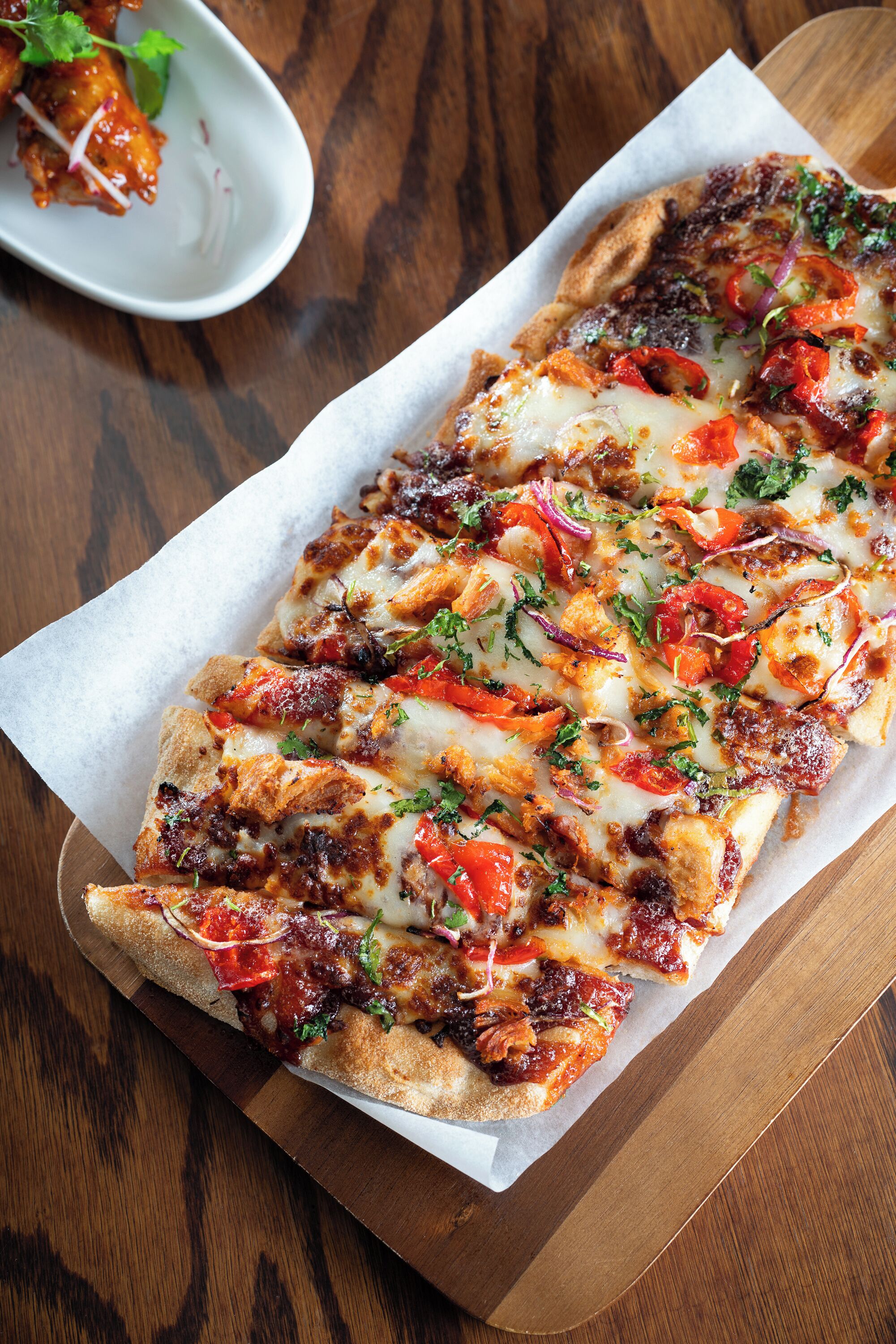 A long rectangular pizza with various toppings on a wooden board.