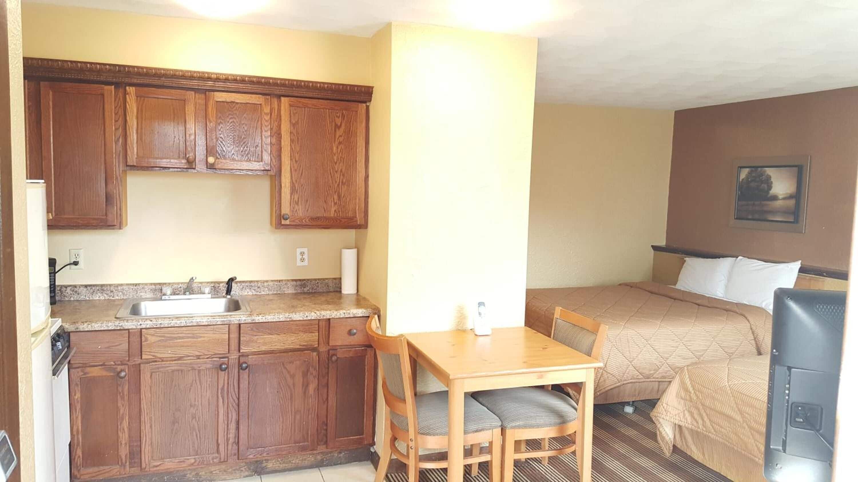 Habitación de hotel compacta con kitchenette, una cama, una mesita y una silla.