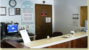 En receptionsdisk på et motel med en computer, et ur og forskellige skilte, heriblandt et for Oakdale Motel og et andet der angiver private whirlpools.