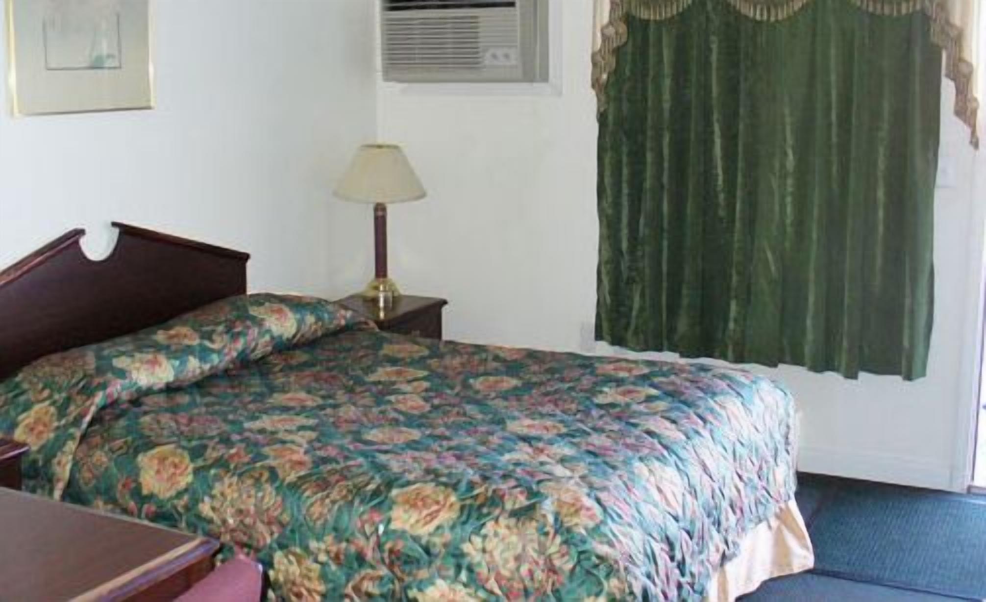 A room with a bed, a nightstand, a lamp, and a window with curtains.
