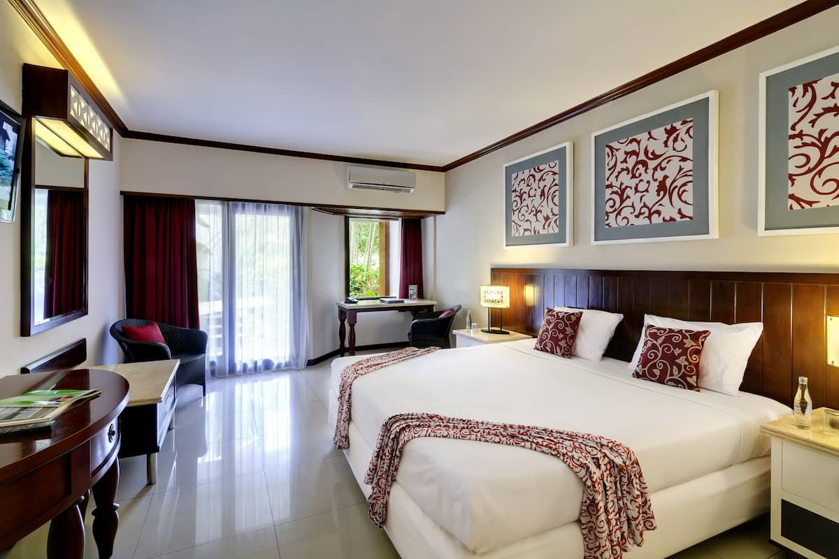 A hotel room with a large bed, a desk with a chair, a computer, and a window with curtains.