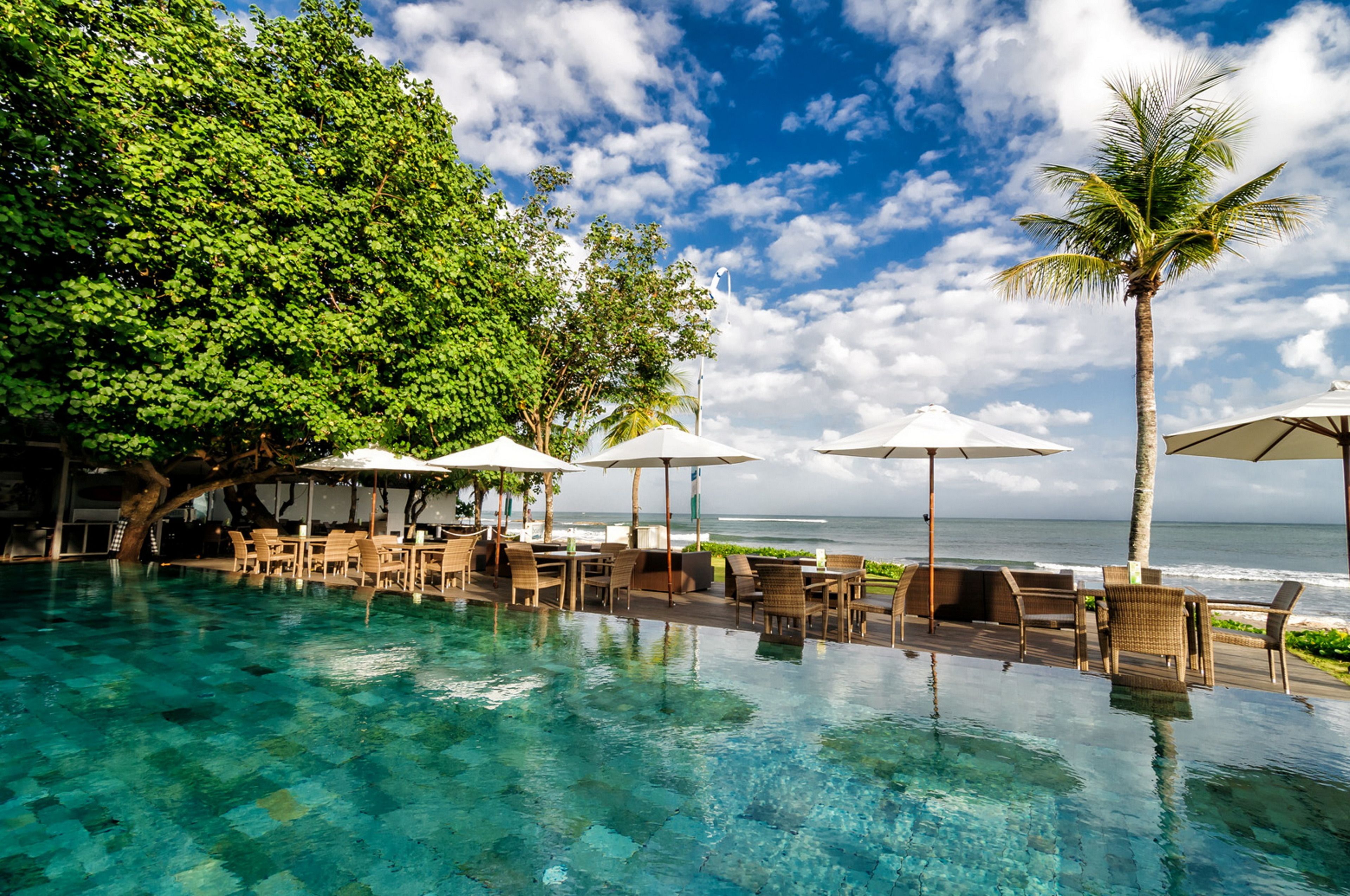 An infinity pool with clear blue water, surrounded by lounge chairs and umbrellas, overlooking the ocean.