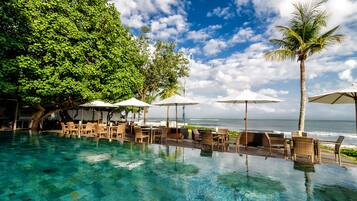 An infinity pool with clear blue water, surrounded by lounge chairs and umbrellas, overlooking the ocean.