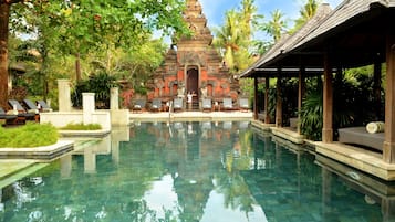 A clear pool with a temple in the background, surrounded by lush greenery and a covered seating area.