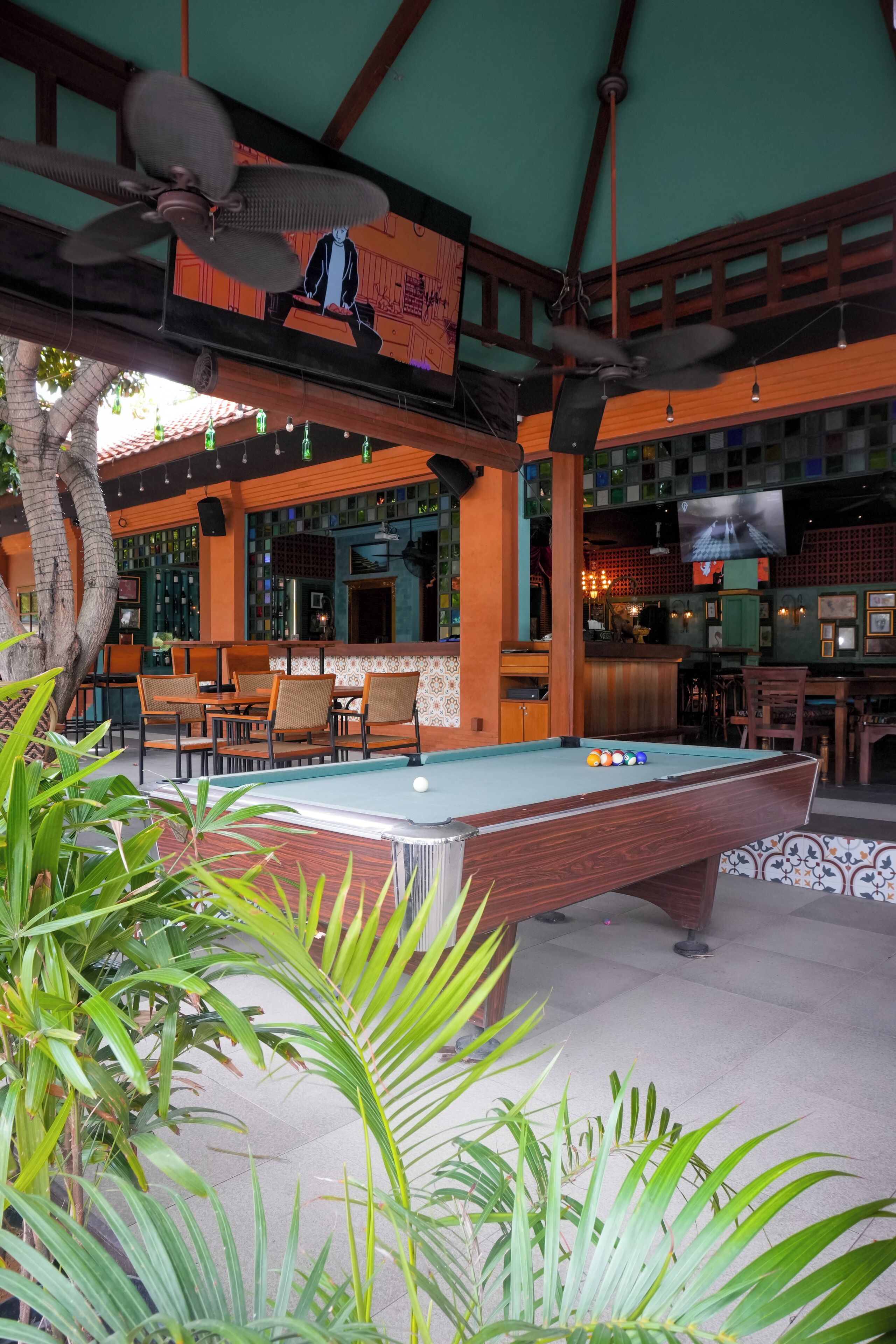 A pool table with chairs, a bar area, and a television screen in a room with wooden beams and green walls.