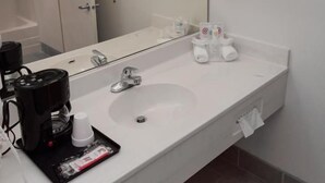 A hotel bathroom with a white sink, a mirror, a towel rack, and a coffee machine. - Sweet Home Inn (Sweet Home)
