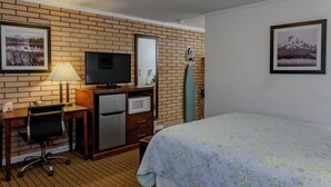 A hotel room with a brick wall, a flat-screen TV, a refrigerator, a microwave, a desk with a chair, a bed with a floral bedspread, and two framed pictures. - Sweet Home Inn (Sweet Home)
