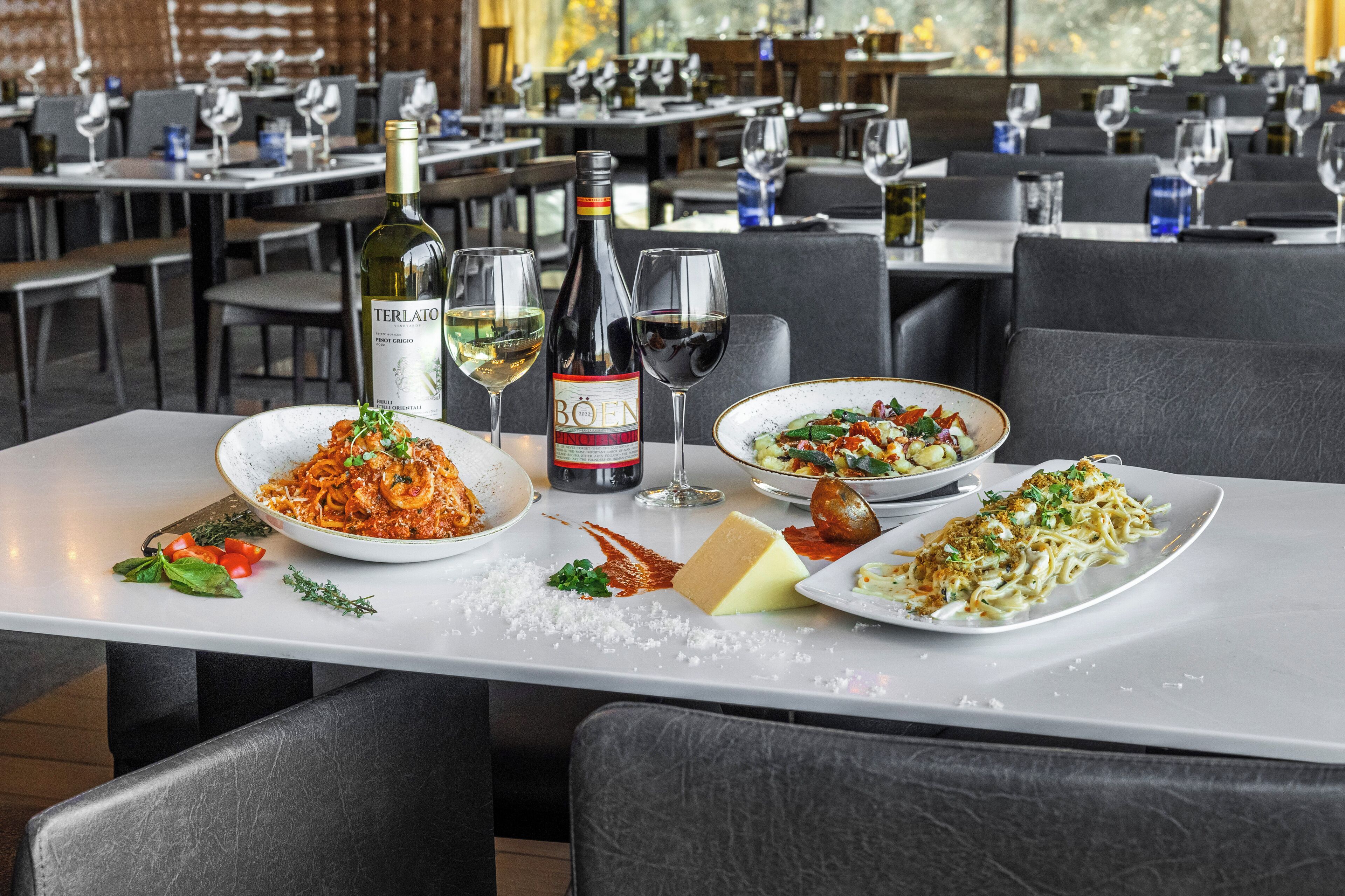 A restaurant setting with a table set for a meal, including plates of pasta and salad, a bottle of wine, and glasses.