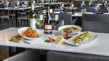 A restaurant setting with a table set for a meal, including plates of pasta and salad, a bottle of wine, and glasses.