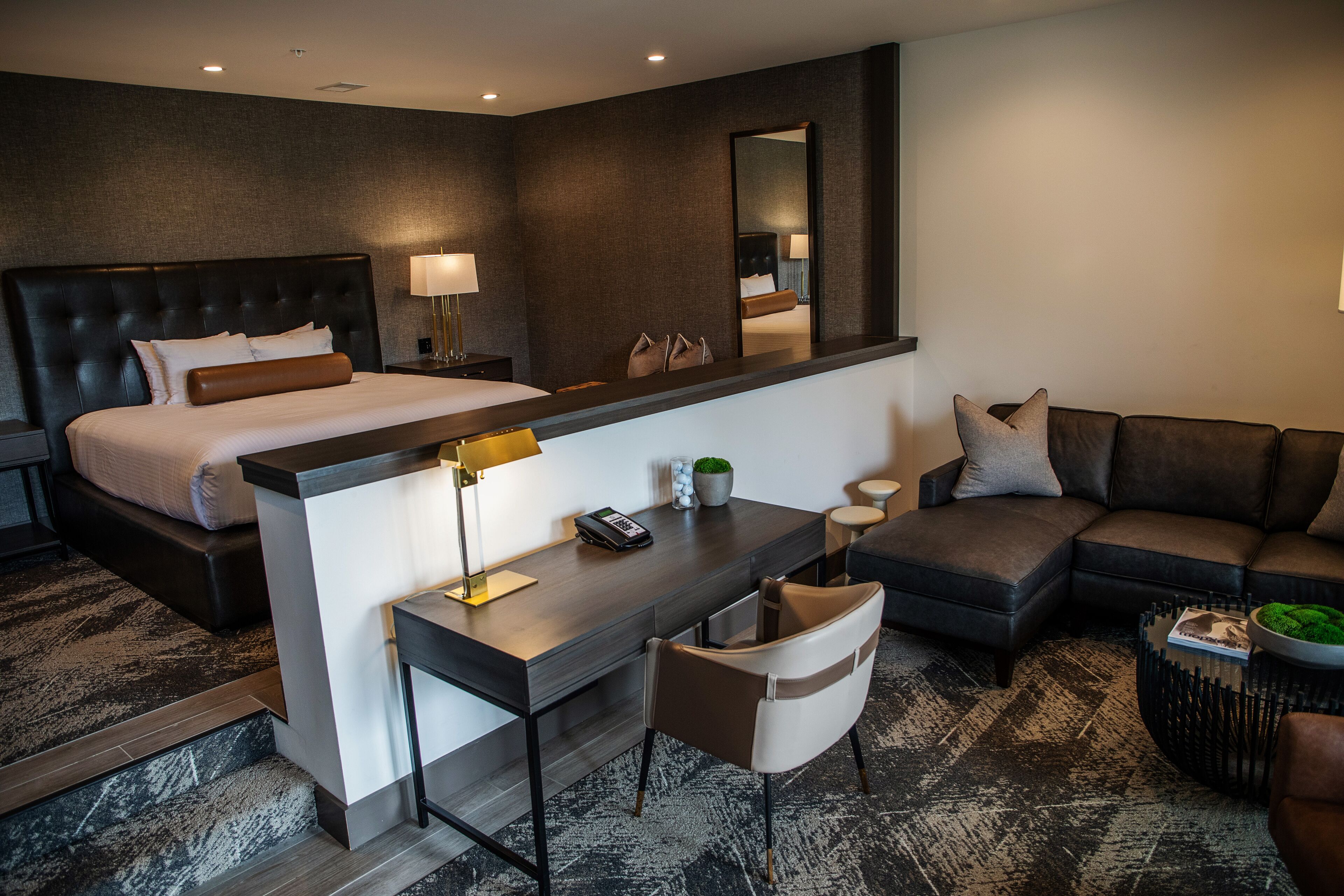 Een moderne hotelkamer met een groot bed, een bureau met lamp, een bank en een spiegel.