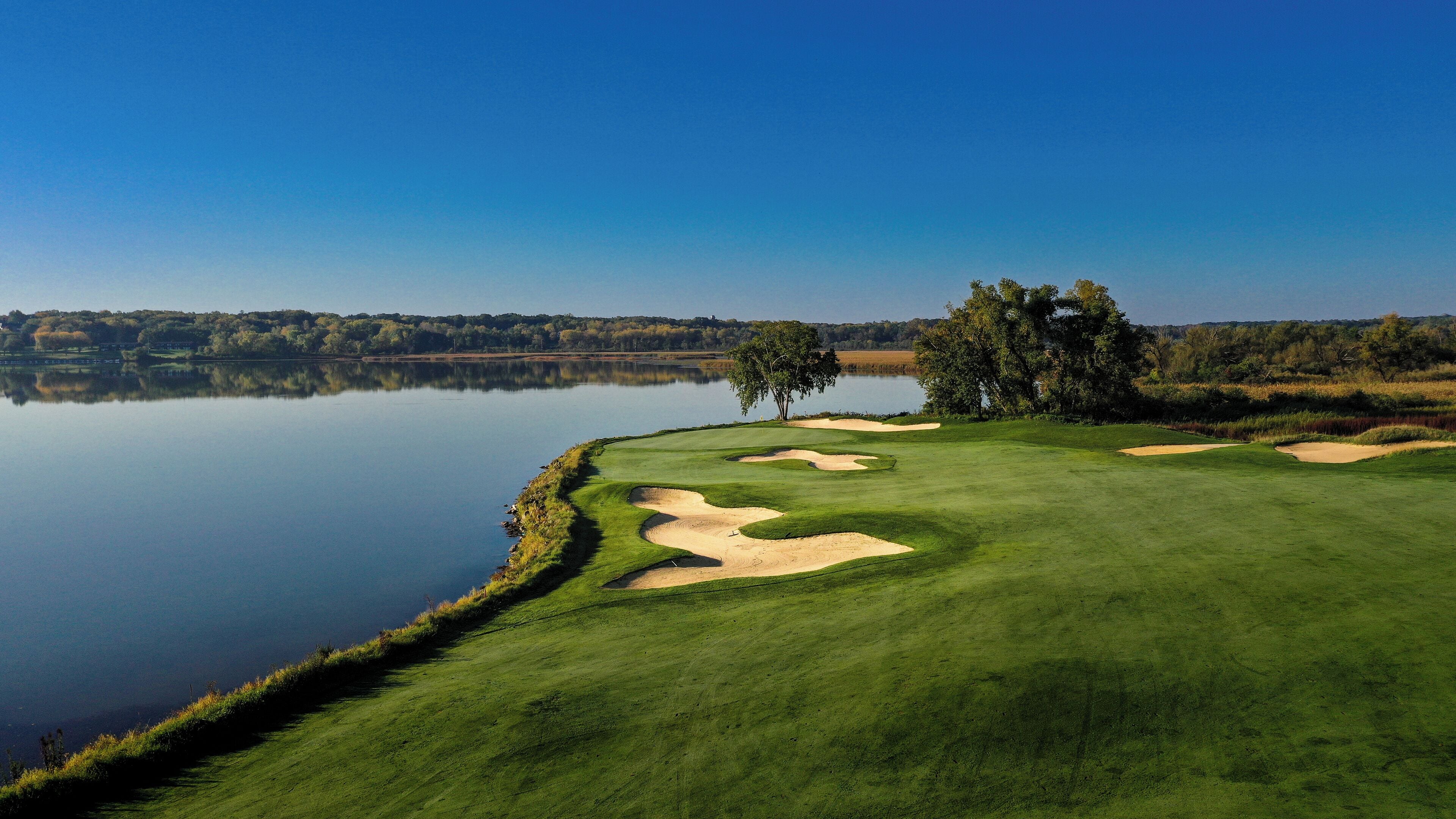 A golf course with a water body, trees, and sand bunkers.