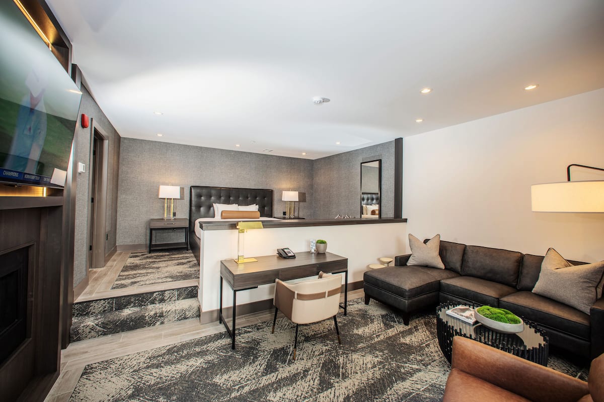 Ein modernes Hotelzimmer mit Bett, Schreibtisch, Sofa, Fernseher und Kamin.