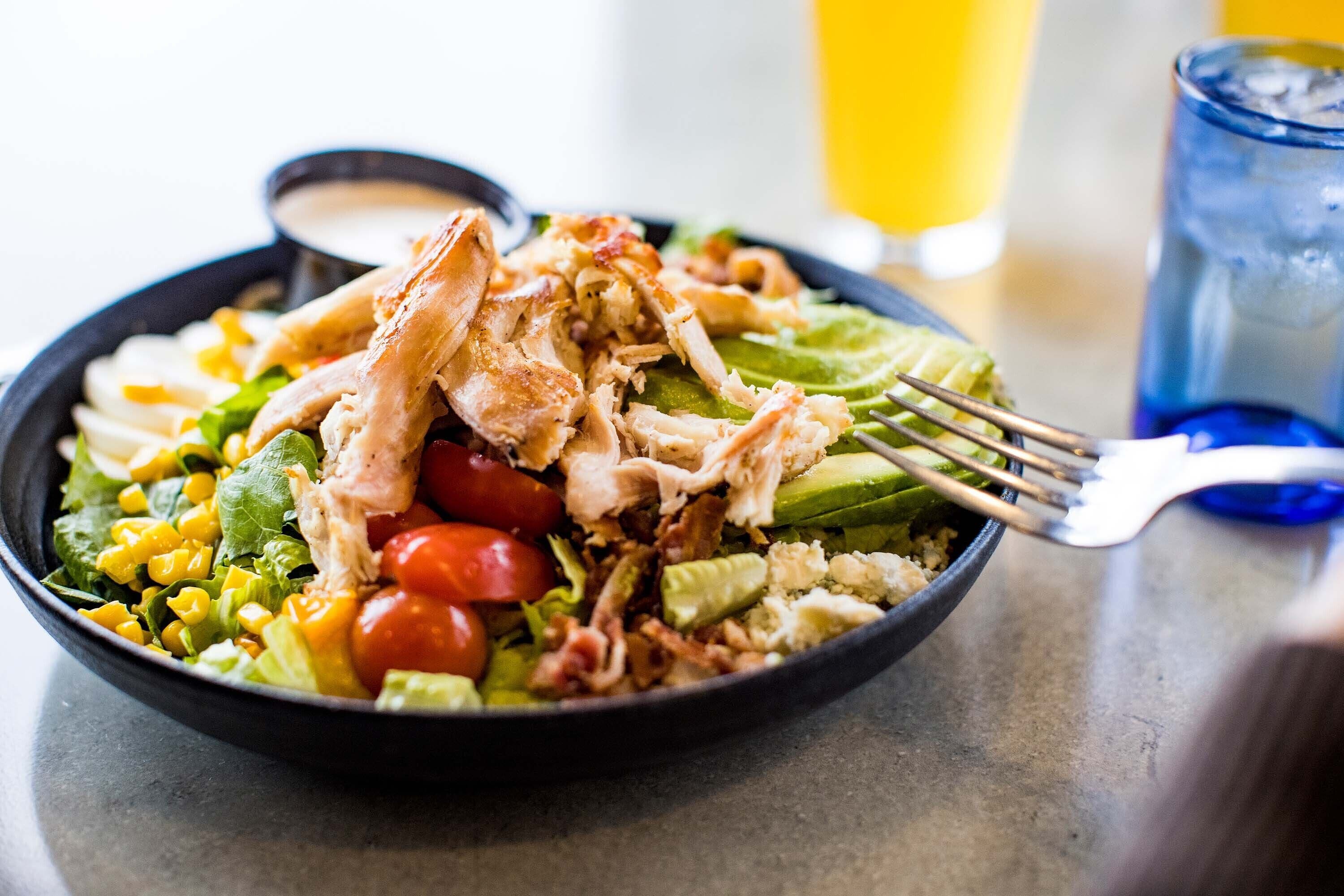 A bowl of salad with various vegetables and shredded chicken, accompanied by a glass of orange juice.