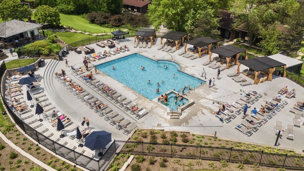 A swimming pool area with lounge chairs and umbrellas, surrounded by trees and a view of a lake. - Destination Geneva National (Lake Geneva)