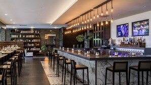 A modern bar area with a long counter, bar stools, and a variety of bottles and glasses. - Destination Geneva National (Lake Geneva)