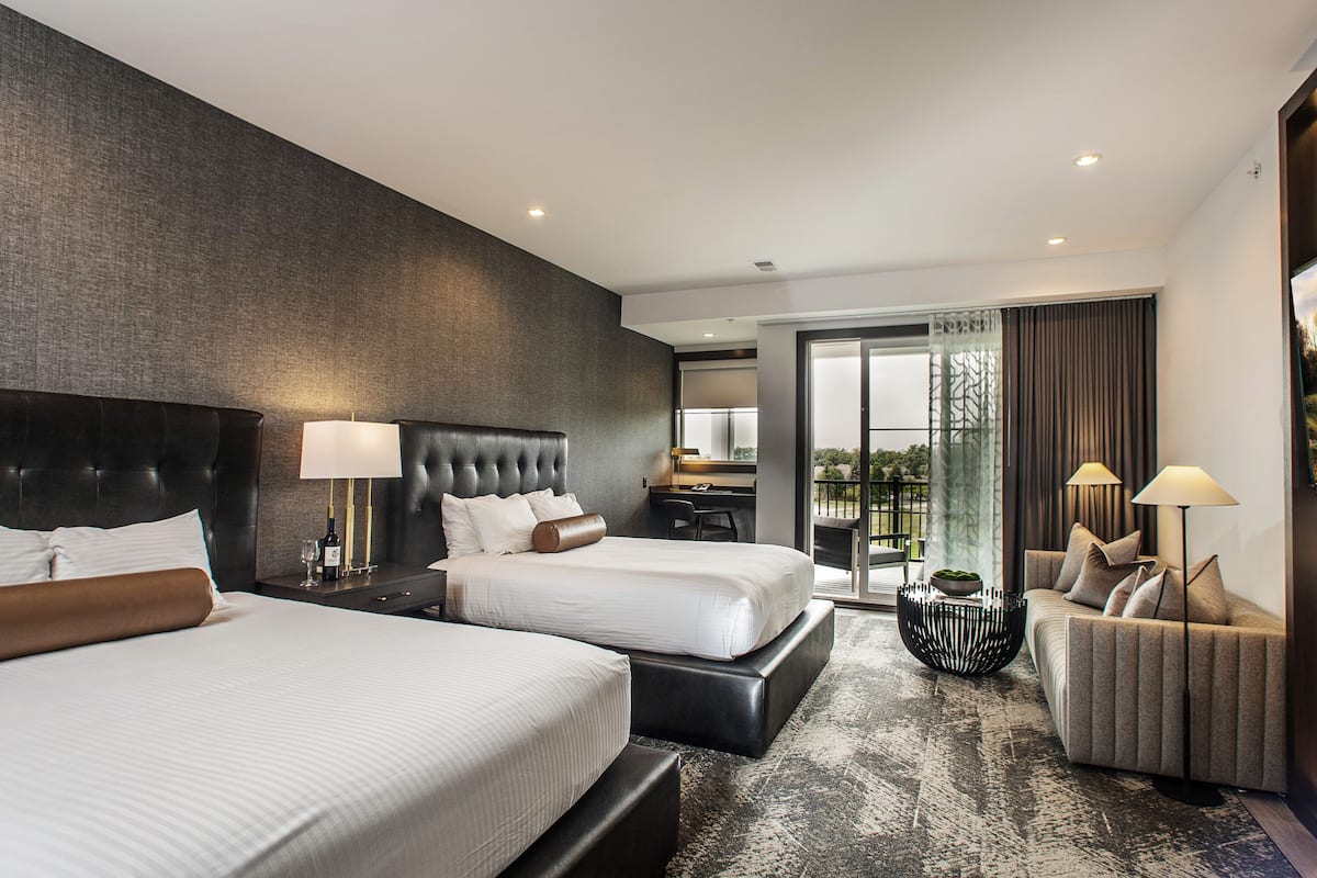 Ein modernes Hotelzimmer mit zwei Betten, einem Schlafsofa, einem Essbereich und einem Balkon mit Blick.