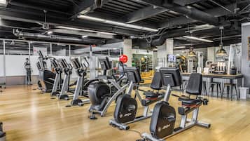 A gym with various cardio machines, a weight bench, and a bar area with stools.