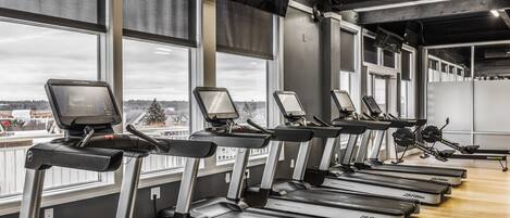 A row of treadmills in a gym with large windows and a view of a snowy landscape.