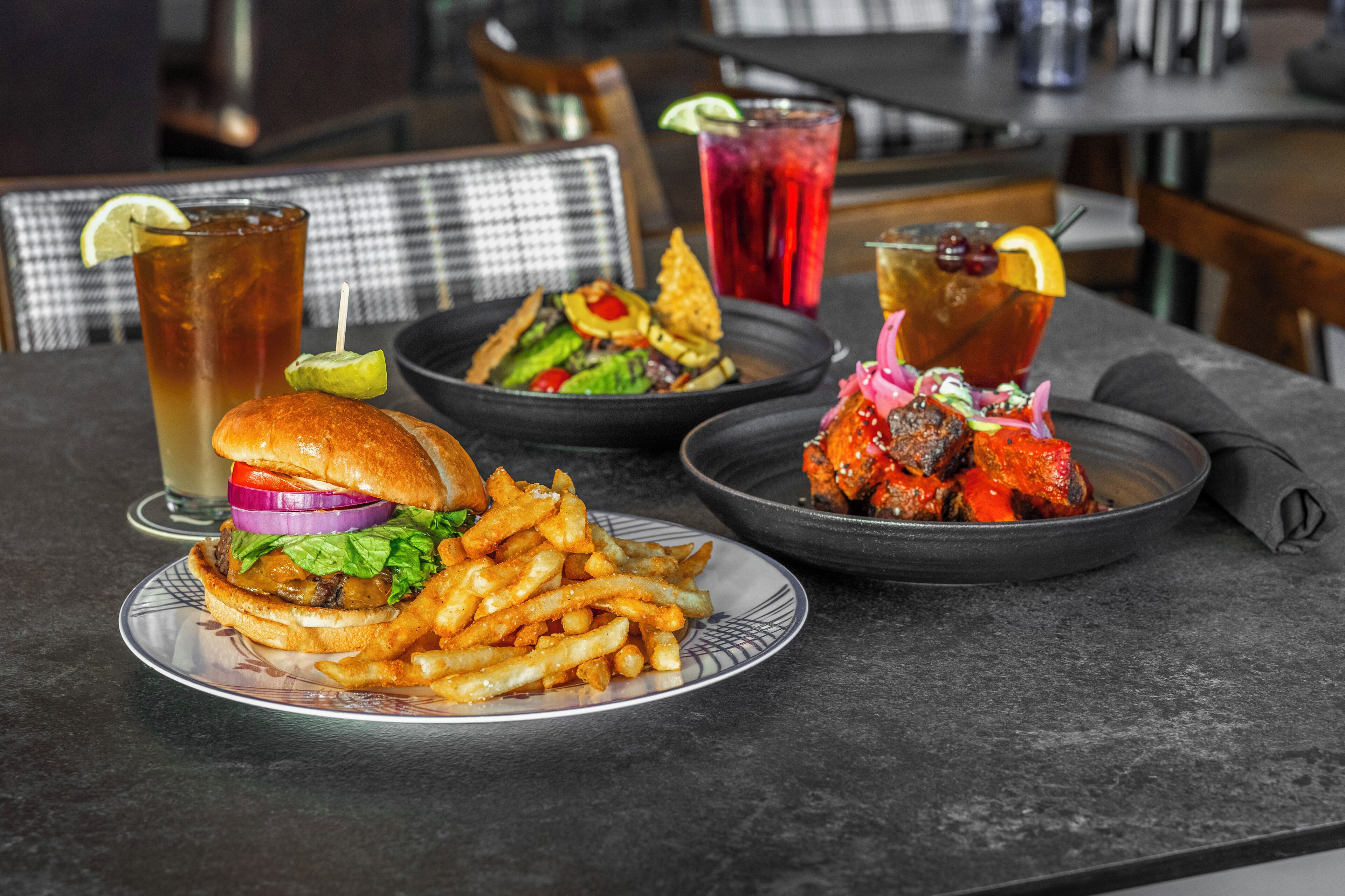 A dining table with a burger, fries, and a seafood dish, along with two drinks.