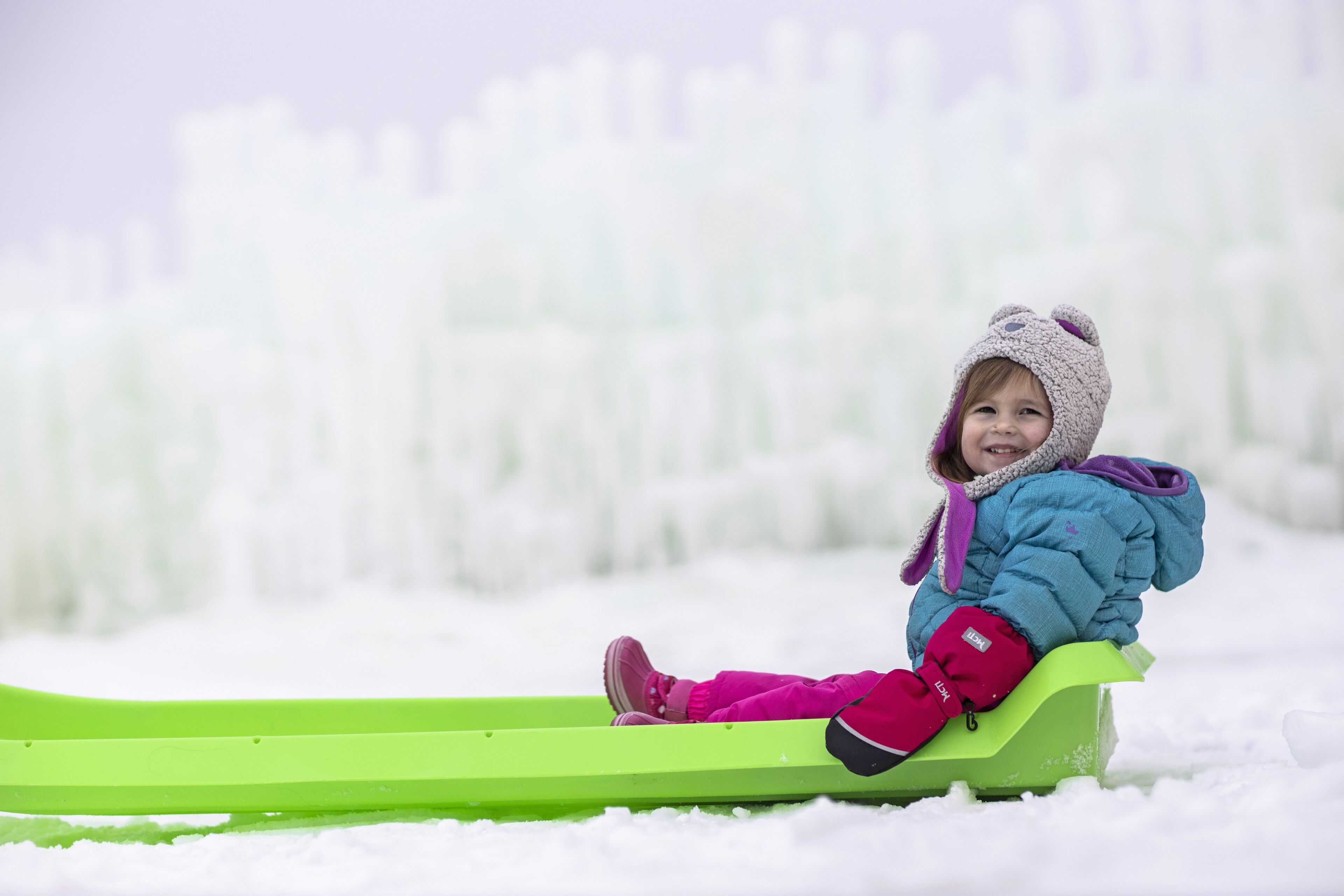 A child sledding on a green sled in a snowy landscape.