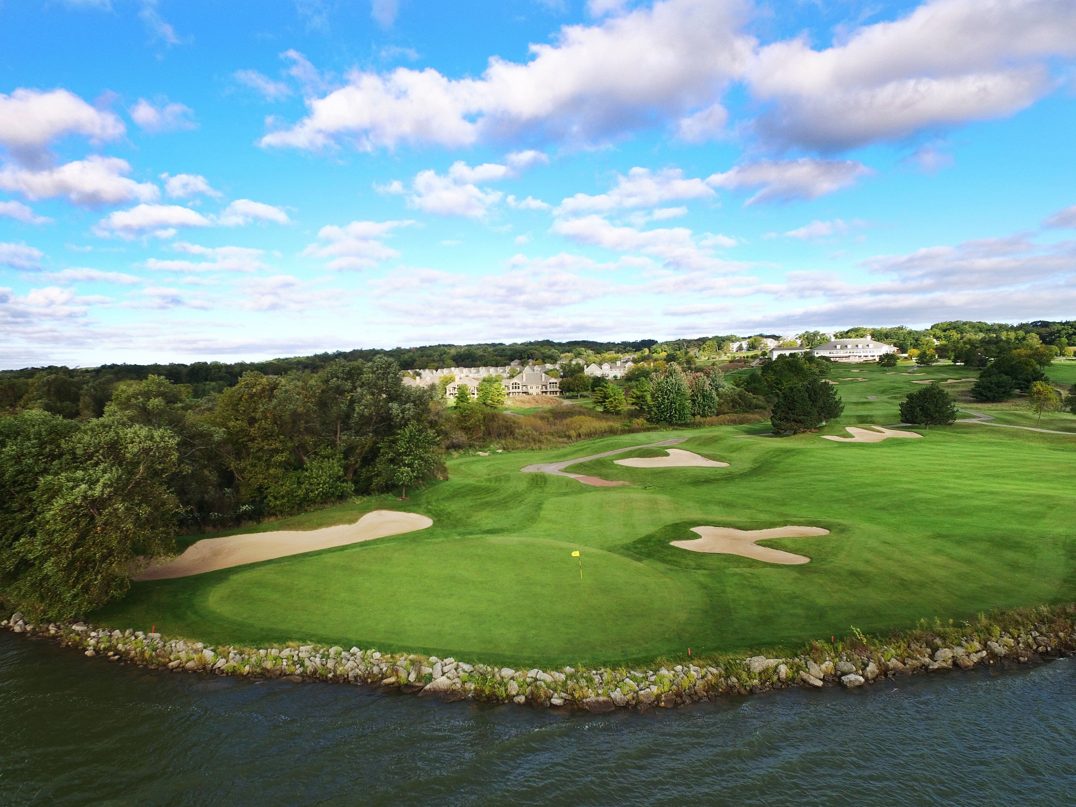 Un parcours de golf avec des bunkers, un plan d’eau et des immeubles résidentiels en arrière-plan.