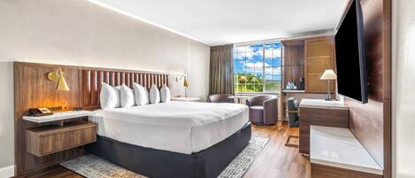 Una habitación de hotel moderna con una cama grande, cabecera de madera, mesitas de noche, un escritorio y un televisor.