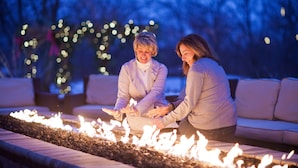 Two people sitting by a fire pit with a couch in the background.