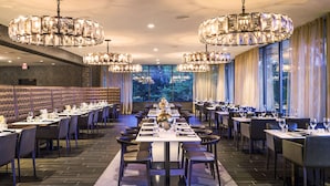 A spacious restaurant with high ceilings, multiple chandeliers, and a long dining table set for a meal.