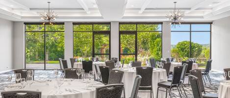 A conference room with round tables, chairs, and large windows offering a view of greenery.