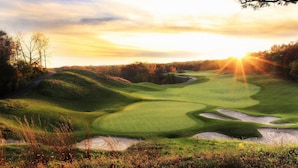 A golf course with sand bunkers, a flag, and a sunset in the background.