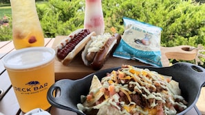 A meal with a hot dog, nachos, and drinks on a wooden table outdoors.