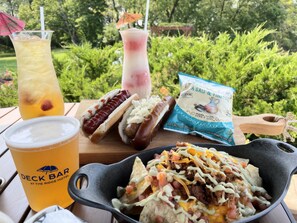 A meal with a hot dog, nachos, and drinks on a wooden table outdoors.