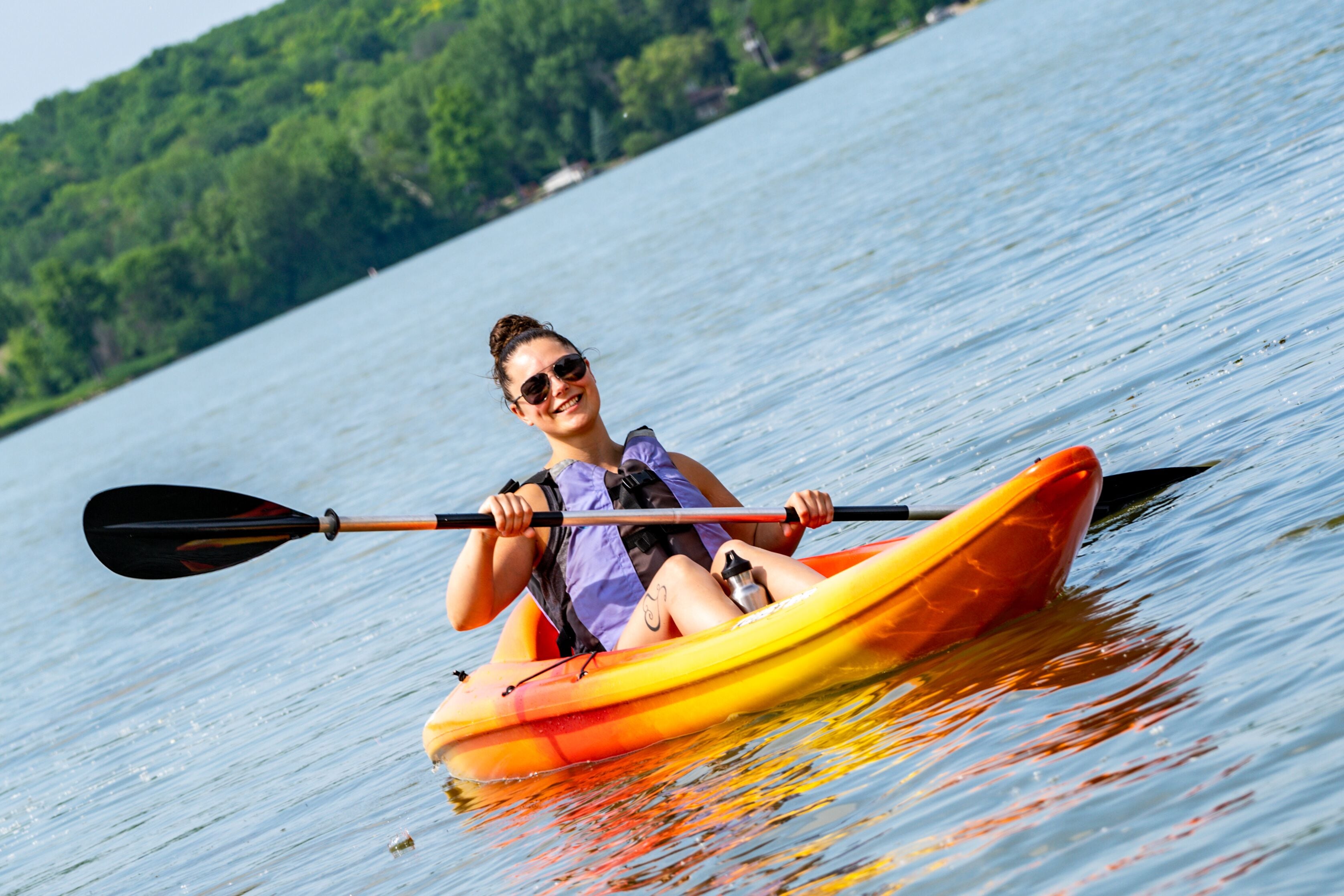 Une personne fait du kayak sur un lac calme, avec une rive boisée en arrière-plan.