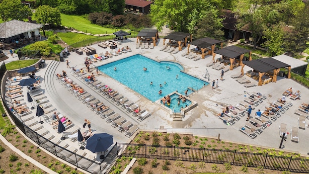 A swimming pool area with lounge chairs and umbrellas, surrounded by trees and a view of a lake.
