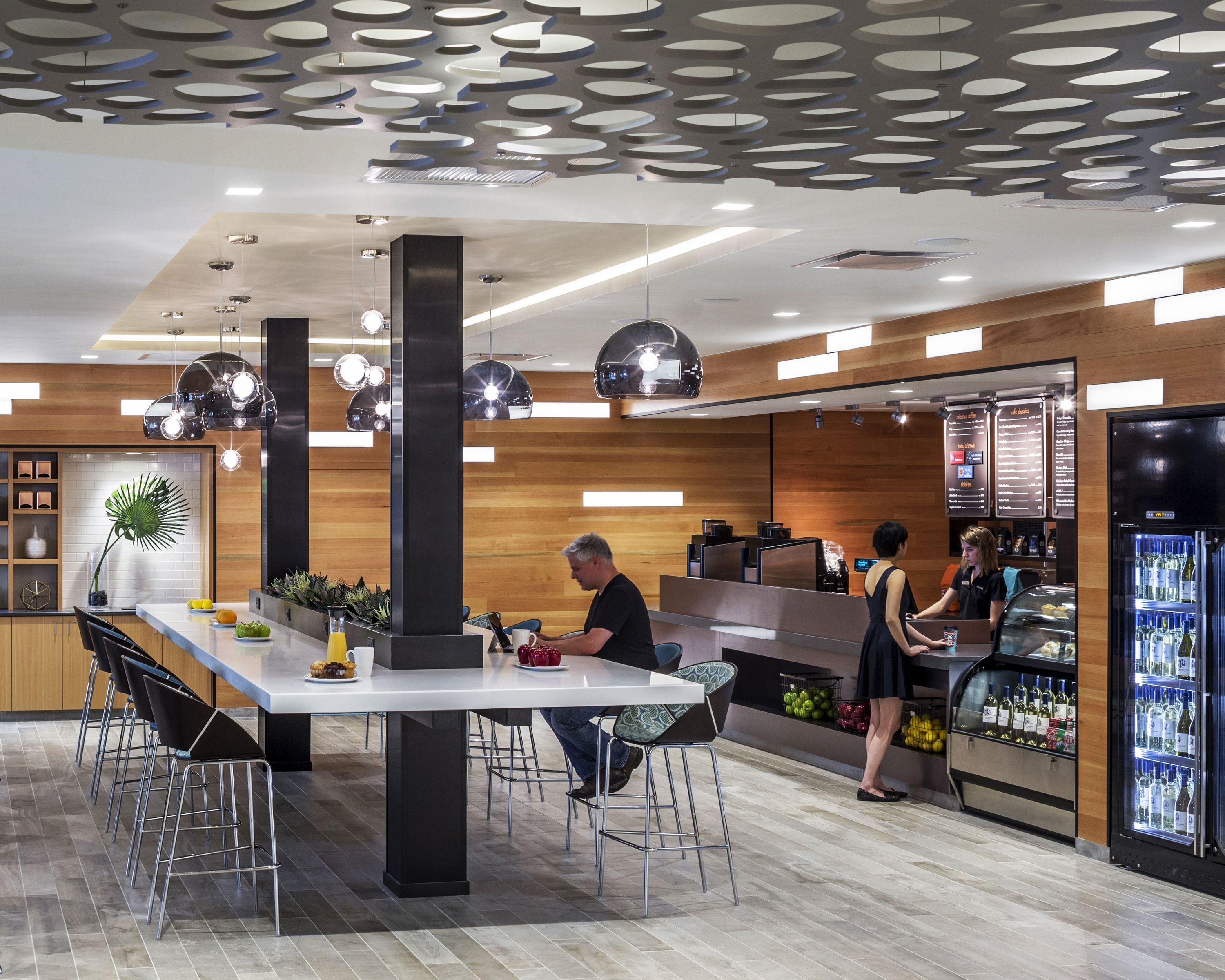 A modern bar area with a long counter, bar stools, and a refrigerated display of beverages.