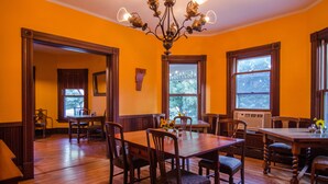 A dining room with wooden tables and chairs, a chandelier, and large windows with views of trees.