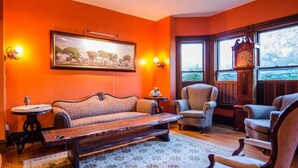 A room with a sofa, armchairs, a wooden coffee table, a clock, and a framed picture on the wall.