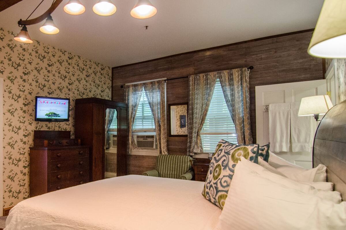 A bedroom with a bed, a TV on a dresser, and a window with curtains.
