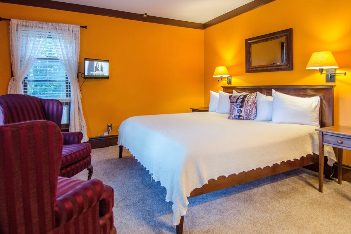 A hotel room with a large bed, two bedside lamps, a television, and a window with curtains.