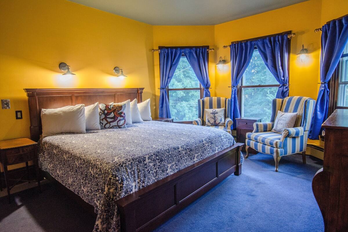 A bedroom with a large bed, two armchairs, a nightstand, and a dresser.