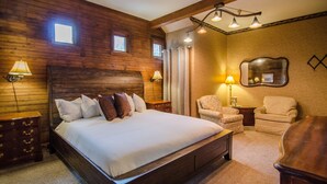 A wooden-paneled bedroom with a large bed, two bedside tables with lamps, a chair, and a mirror on the wall.