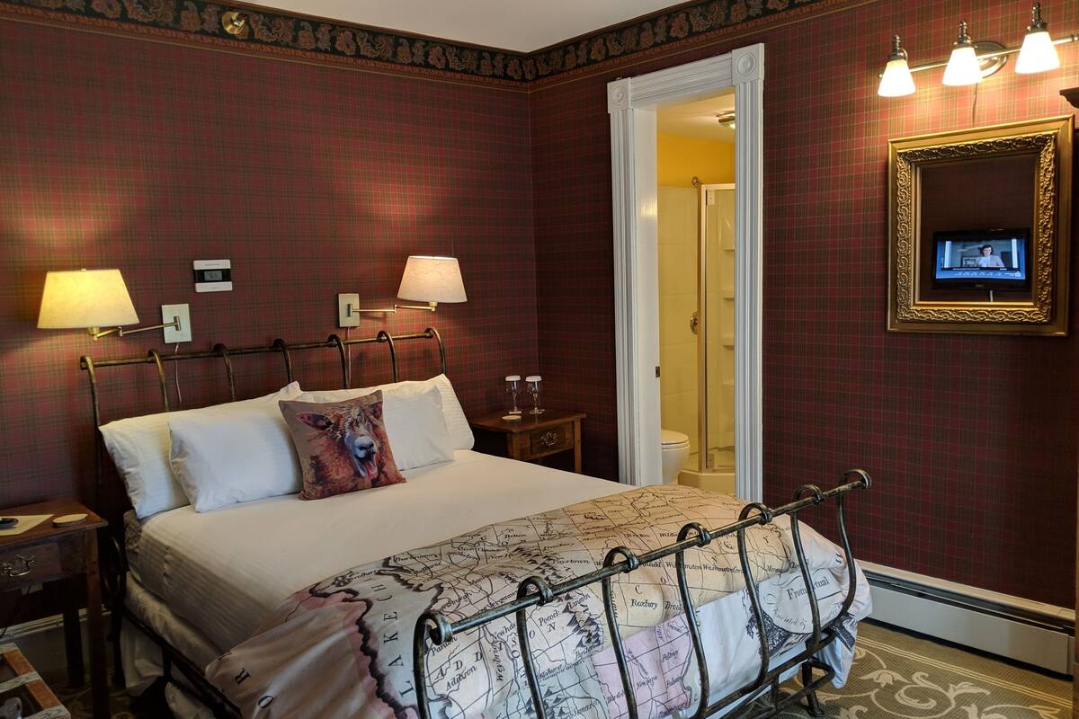A hotel room with a large bed, two bedside lamps, a television on the wall, and a map-themed bedspread.