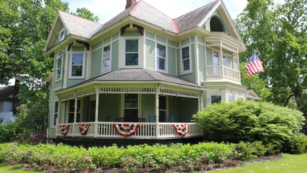 A two-story house with a porch, a chimney, and an American flag.